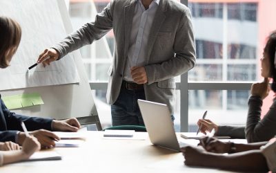 Skilled 30s caucasian leader in eyeglasses coaching interested business people, giving educational workshop presentation in office. Concentrated employees listening to professional coach at workshop.